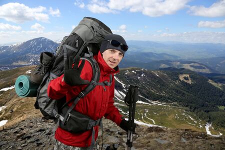 the happy traveler equipped with a red jacket on the hillside raised in greeting handの写真素材