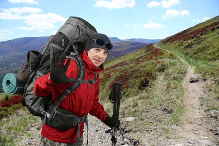 the happy traveler equipped with a red jacket on the hillside raised in greeting handの写真素材
