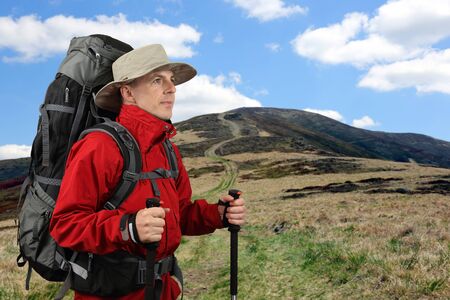 the equipped with traveler in a red jacket with Hiking poles looks into the distanceの写真素材