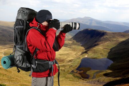 equipped with the traveler photographer in a red jacket takes pictures of natureの写真素材