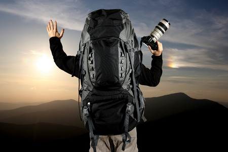 the a traveler with a large backpack and hands with the camera at sunsetの写真素材