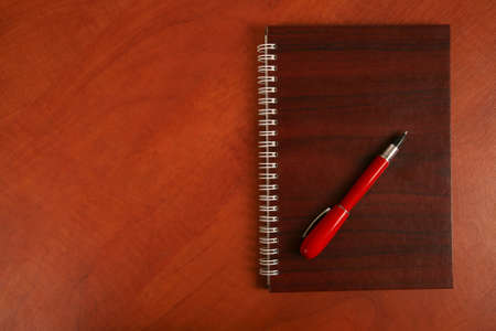 the notebook and a red pen lying on wooden deskの写真素材