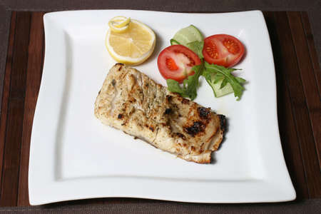 the fried piece of fish in lemon juice with vegetablesの写真素材