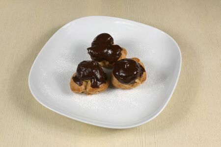 Profiteroles with chocolate icing on a plate with powdered sugarの写真素材
