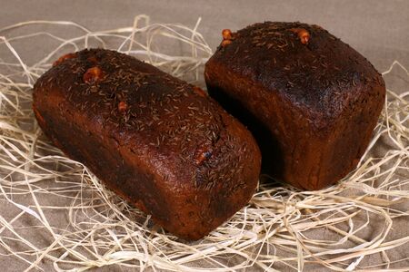 two dark bread stuffed with cheese lying in straw on grey linen tableclothの写真素材