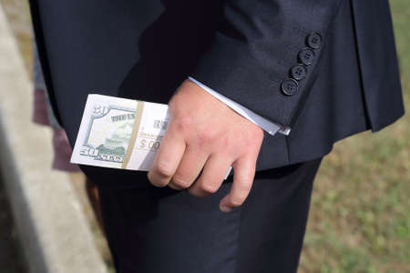 man in a nice suit holding in his left hand banknotes close up