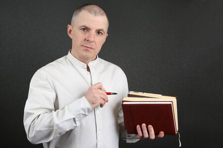 man in the bright shirt holding a stack of books and pointing to them with a penの写真素材