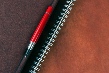 the notebook and a red pen lying on wooden deskの写真素材