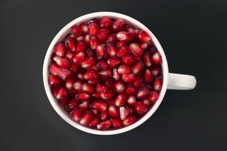 pomegranate seeds in a white cup on a dark background