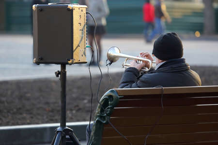 street musician sitting on the bench and plays the trumpet