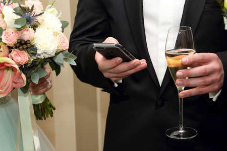 the groom with mobile and glass in handの写真素材