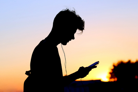 silhouette of a man with a mobile phone and headphones at sunsetの写真素材