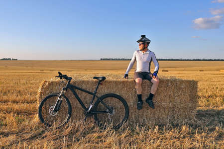 the cyclist with the bike resting on straw harvested fieldの写真素材