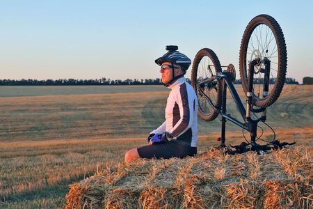 the cyclist with the bike resting on straw harvested fieldの写真素材