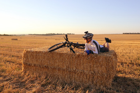 cyclist with the bike resting on straw harvested fieldの写真素材
