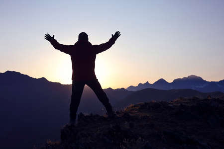 Silhouette tourist with arms raised standing on the mountain at dawnの写真素材