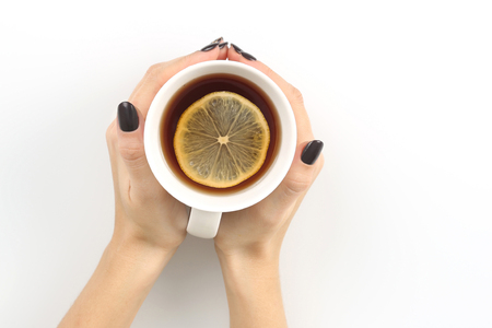 Female hand with a Cup of tea with lemon on a white table topの写真素材