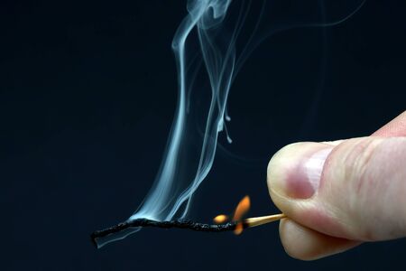 Burning and smoking wooden match in hand on dark backgroundの写真素材
