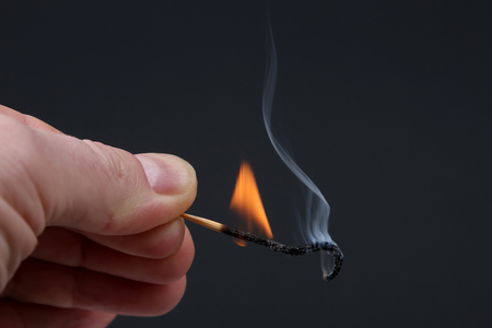 Burning and Smoking wooden match in hand on dark background