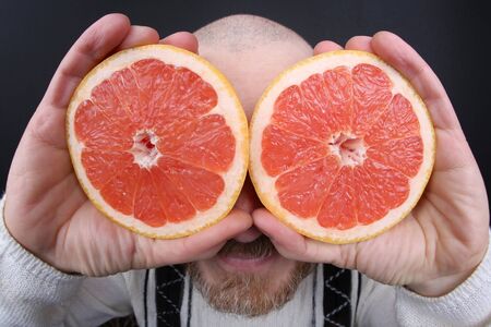 bearded man with a cut grapefruit in his handsの写真素材
