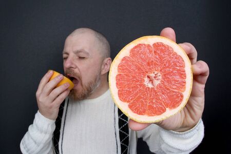 bearded man with a cut grapefruit in his handsの写真素材