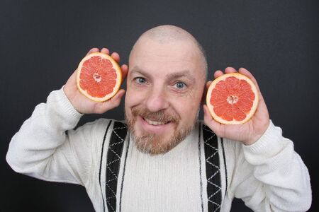 smiling bearded man with a cut grapefruit in his handsの写真素材