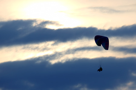 Paragliders flying on the wing against the sun in the clouds