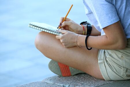 girl draws in a notebook sitting on the pavementの写真素材