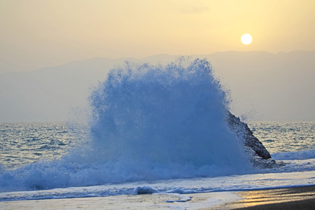Sea wave beats on the rock against the sunset