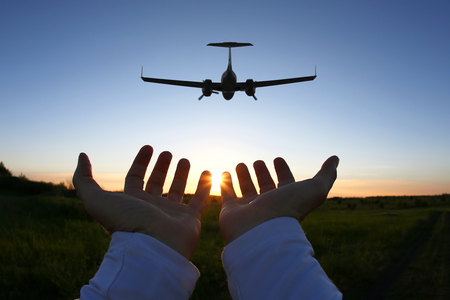 raised hands on the background of a passenger plane flying at sunset