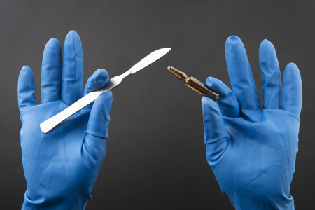 Medical scalpel and vial for injection in hands wearing blue glovesの写真素材