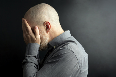 sad man with his hands closed face turned away from the lightの写真素材