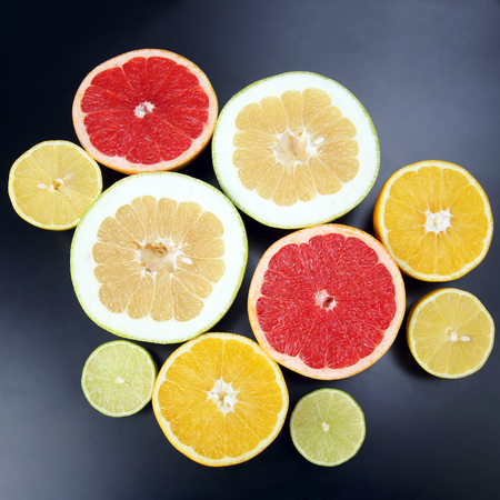 cut pieces of different citrus fruits on dark backgroundの写真素材