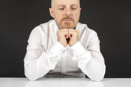 happy bearded man in white shirt with eyes closed sitting at white tableの写真素材