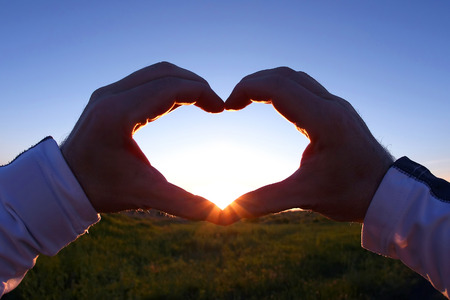 clasped hands in heart shape on a background sunset. the relation of man to natureの写真素材