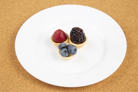 Blackberry, blueberry and strawberry in a waffle basket on a white plate. Vitamins and wholesome...