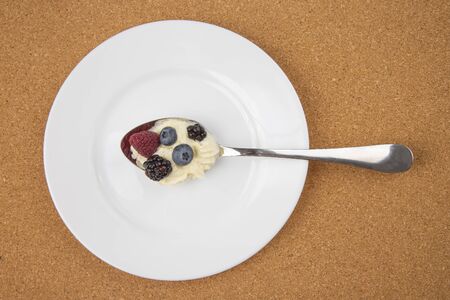 Raspberries, blackberries, blueberries with cream in a spoon on a white plate. Vitamins and...