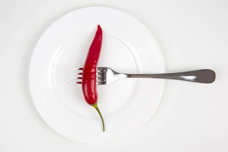 red hot pepper on a fork on a white plate. spices and vegetative food
