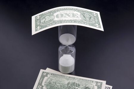 Dollar bills lie near the hourglass. Time is money. The salary. Business solutions in time....