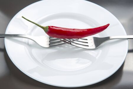 red hot pepper on a fork on a ceramic plate. spices and vegetative foodの写真素材