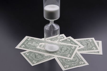 Dollar bills lie near the hourglass. Time is money. The salary. Business solutions in time. Hourglass time measurementの写真素材
