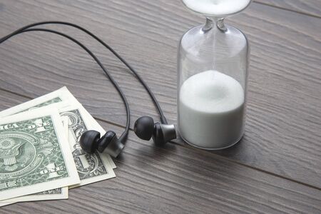 Hourglass, money and headphones are on the table. Business office items. Time is money. Business...