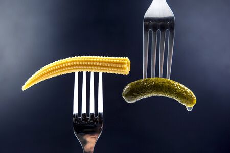 pickled cucumber and corn on a fork close-up on a dark blue background. food and vegetablesの写真素材