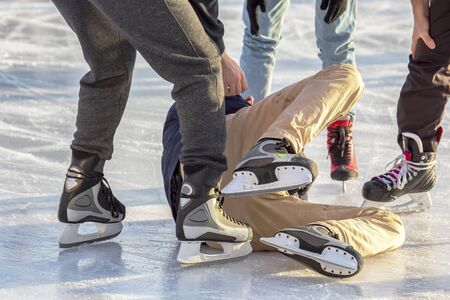 people on an ice rink help a fallen person to rise. injuries and sports on the ice rink. fall and health in winter activitiesの写真素材