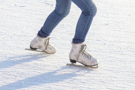 legs of a girl in blue jeans and white skates on an ice rink. hobbies and leisure. winter sportsの写真素材