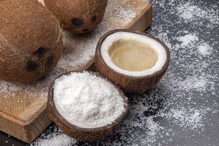 cut fresh coconut with real coconut milk on a dark background of coconut flakes. vitamin fruits....