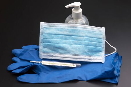 Medical mask, sterile gloves, thermometer and alcohol disinfectant on a dark background. pandemic...