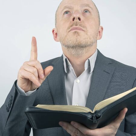 man in a business suit is reading the bible. man raised a finger up