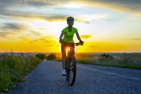 Beautiful girl cyclist riding a bike on the road towards the sunset.の写真素材