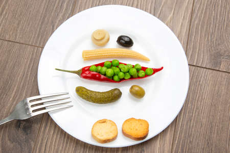 salad of canned and pickled olives, mushrooms, corn, peas, cucumber and red pepper on a white plate....